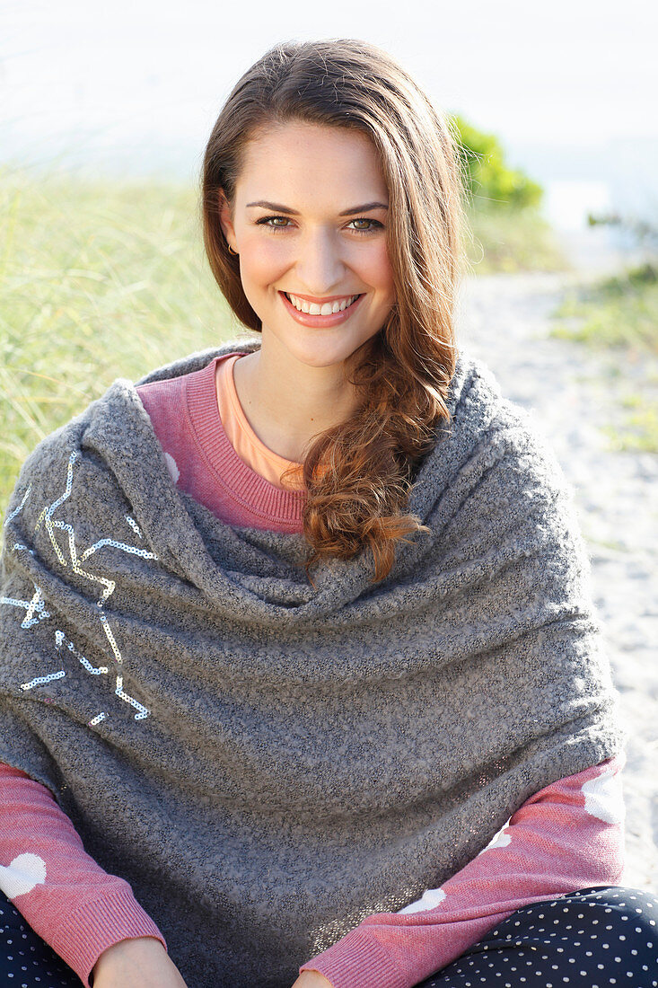 A brunette woman wearing a grey shawl and a pink knitted jumper with heats