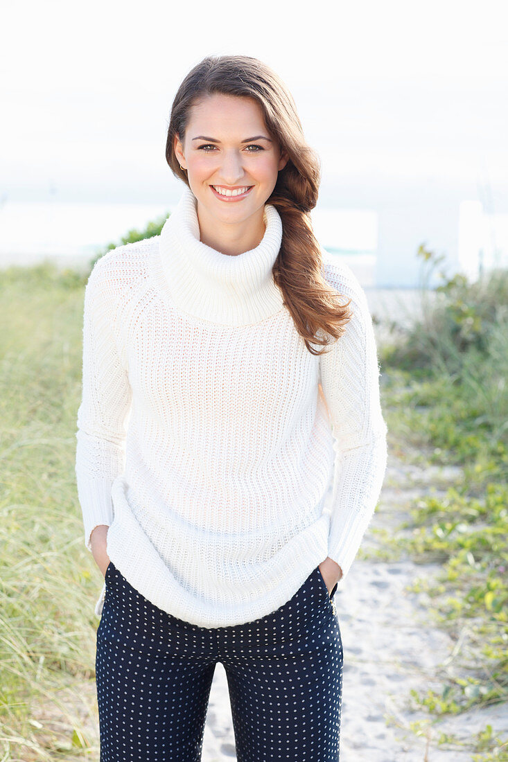 A brunette woman wearing a white knitted jumper and dark trousers