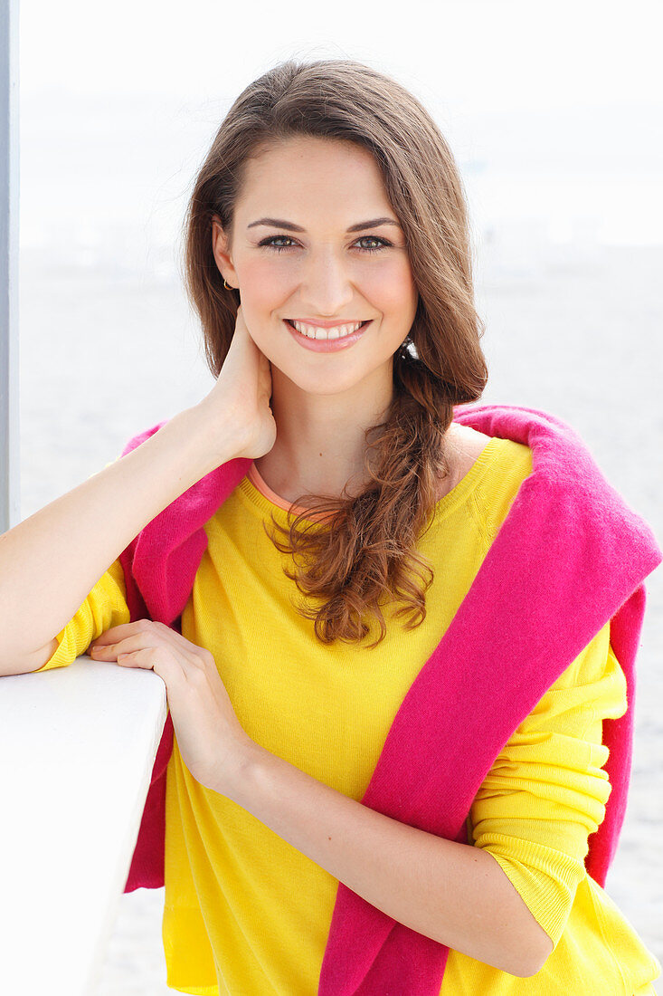 Brünette Frau in gelbem Pullover und pinkfarbenem Pulli über den Schultern