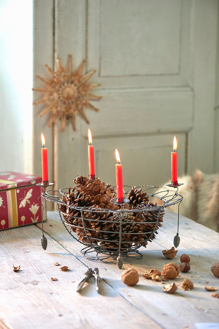 Apples in wire basket with four lit red candles on rim