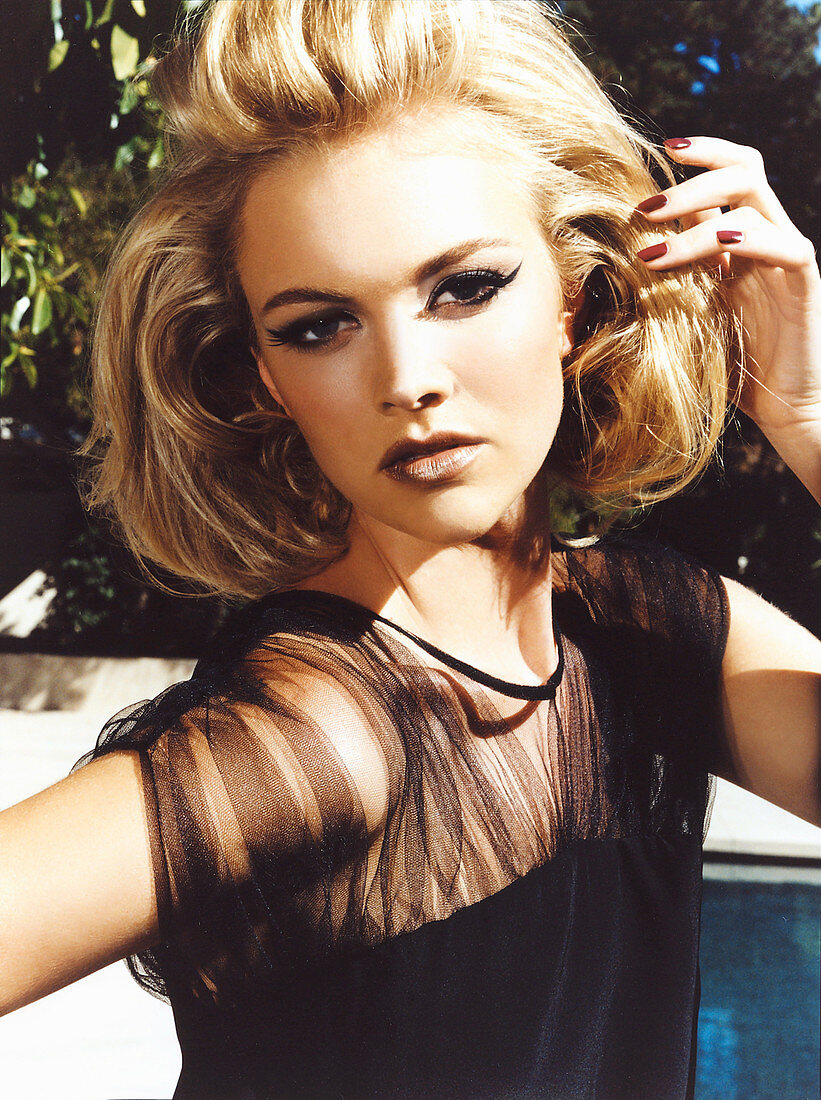 A young blonde woman in a garden by a pool posing in a black evening dress