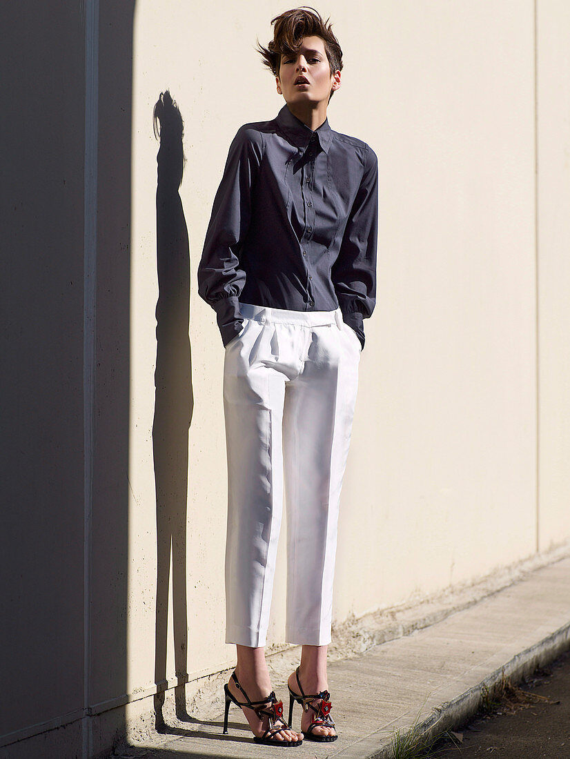 A young brunette woman with short hair wearing white trousers and a purple blouse