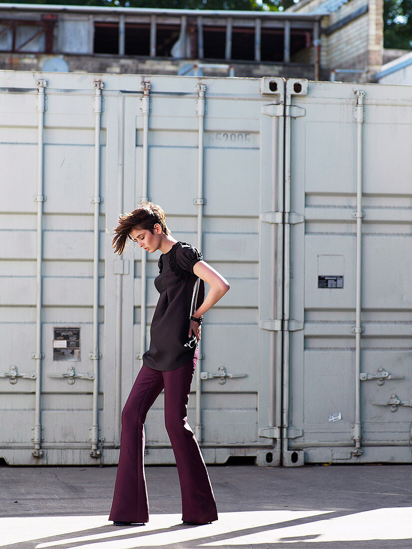 A young brunette woman with short hair wearing purple trousers and grey top