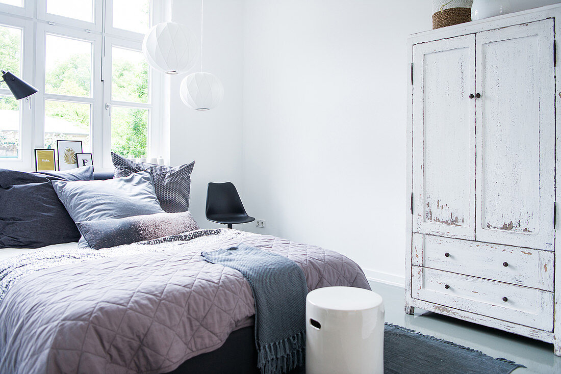 Doppelbett mit Tagesdecke und Kleiderschrank mit abgeblätterter Farbe im Schlafzimmer