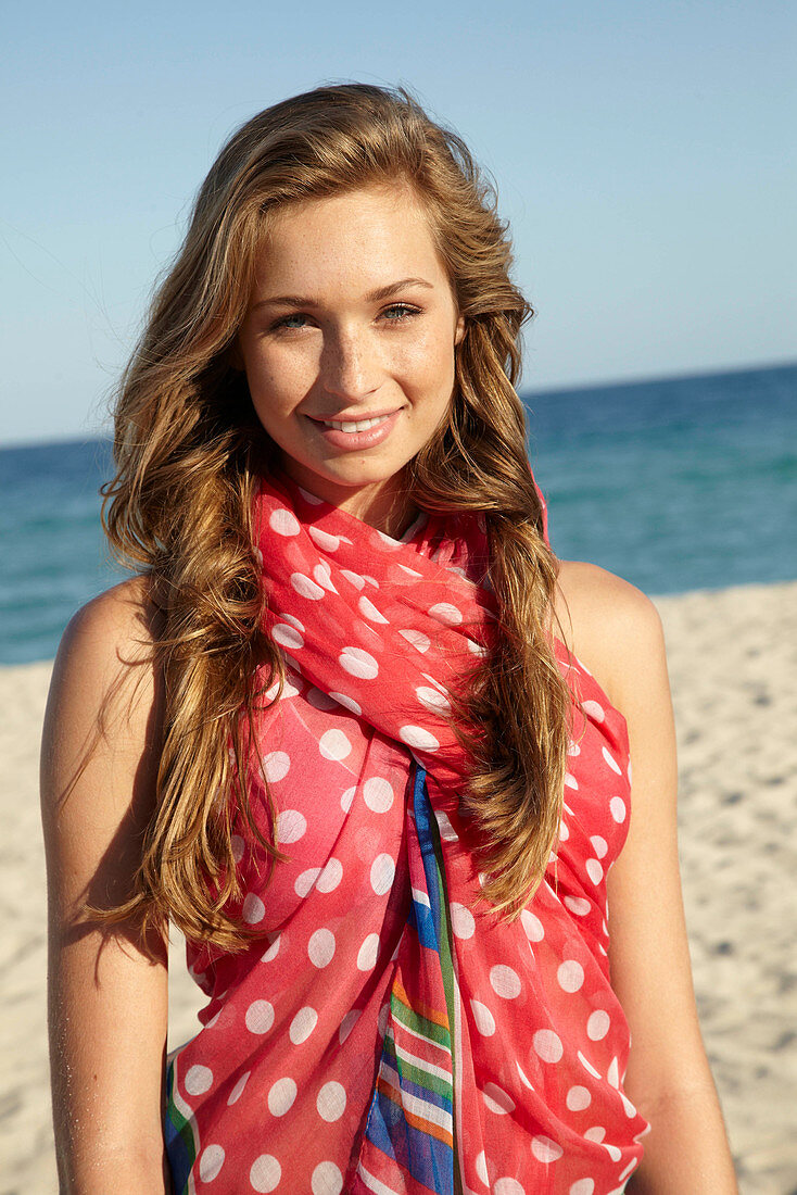 A young blonde woman by the sea wearing a beach towel