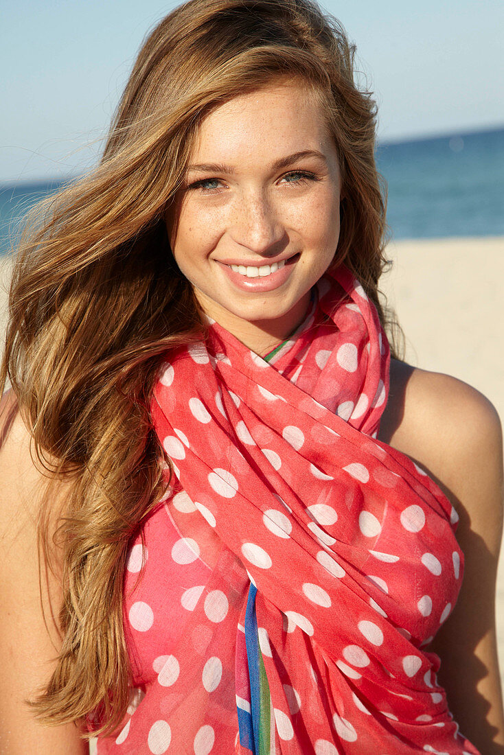 A young blonde woman by the sea wearing a beach towel