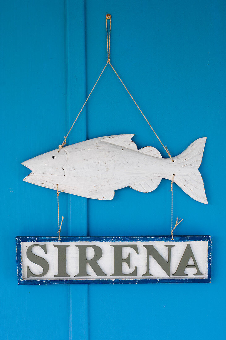 Anhänger mit Holzfisch und Schild an blauer Wand