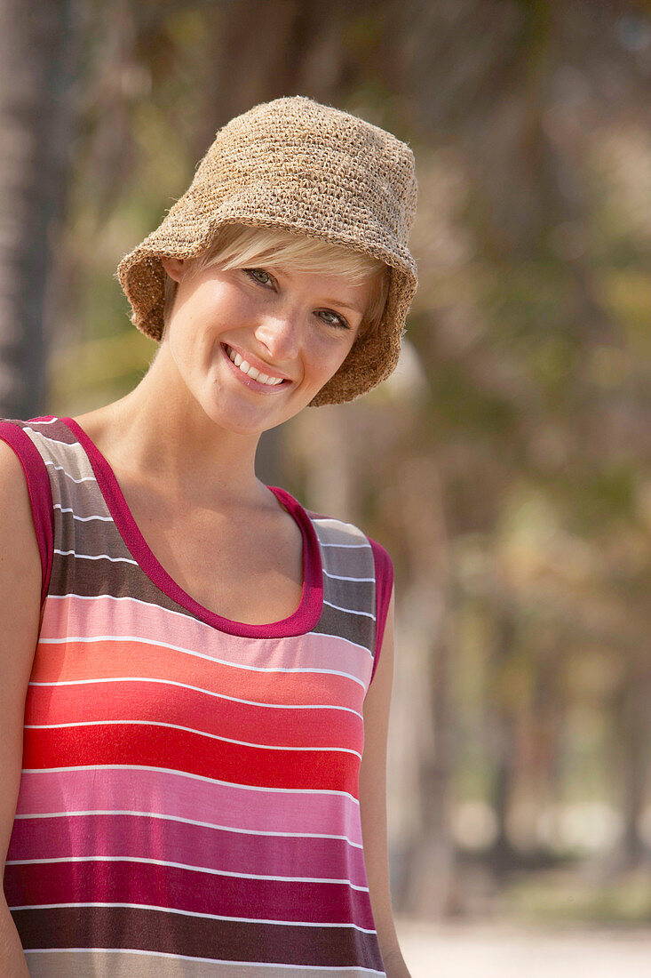 A mature blonde woman with short hair outside wearing a striped top and a hat