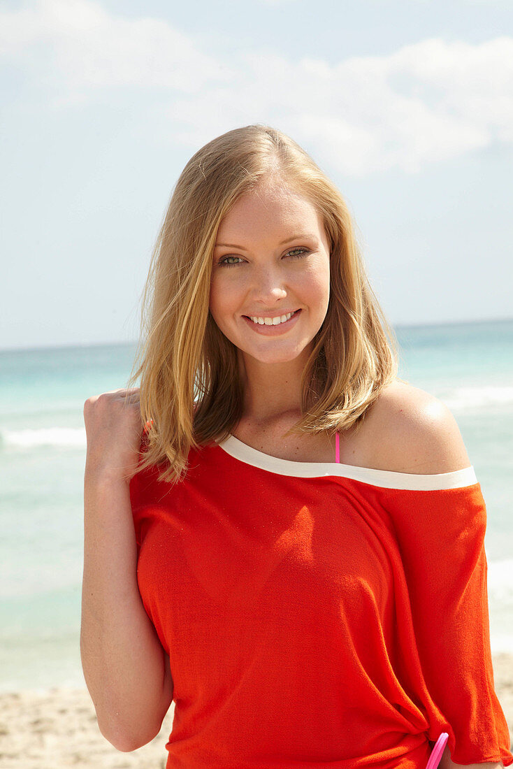A young blonde woman on a beach wearing an orange top