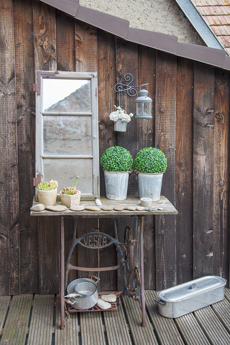 Alter Nähmaschinengestell mit Topfpflanzen, Steinen und Fenster auf Terrasse