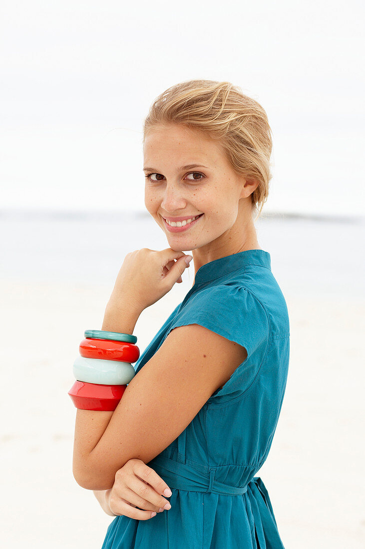 A young blonde woman on a beach wearing a blue summer dress