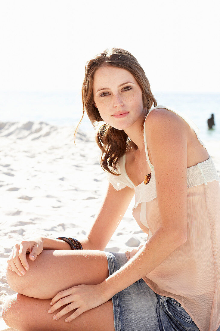 A young brunette woman on a beach wearing a beige top