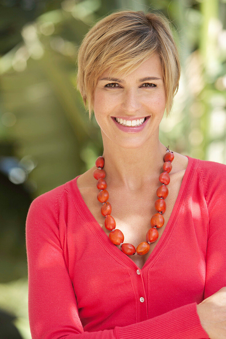 A mature woman with short blonde hair outside wearing a red shirt
