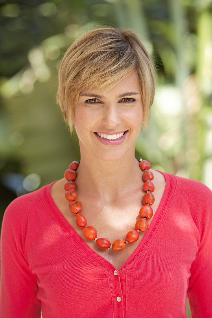 A mature woman with short blonde hair outside wearing a red shirt