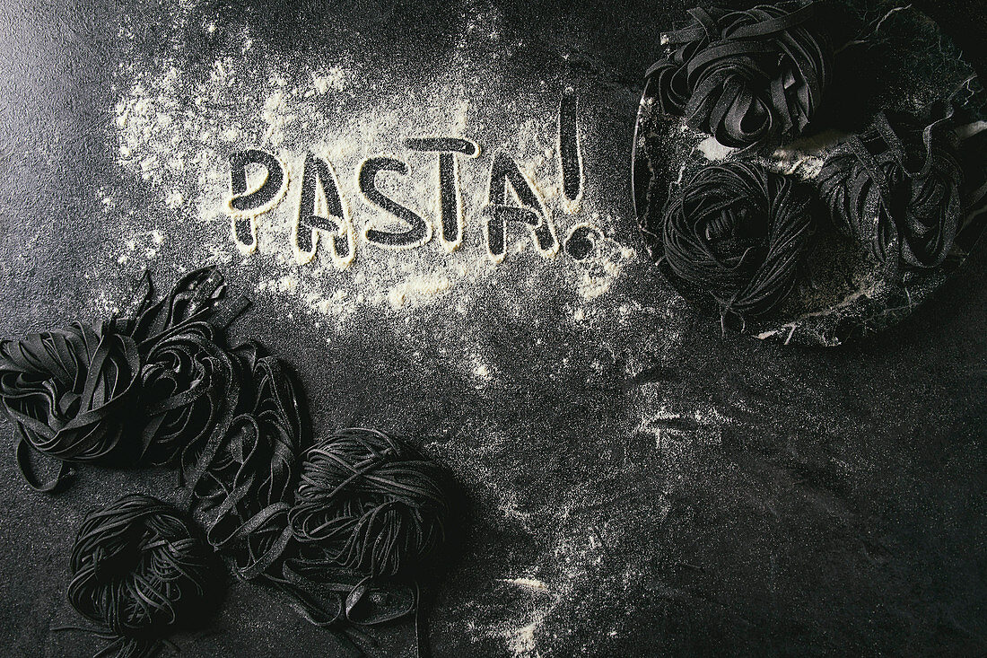 Frische Sepianudeln und das Wort 'Pasta' in Mehl geschrieben auf schwarzem Untergrund