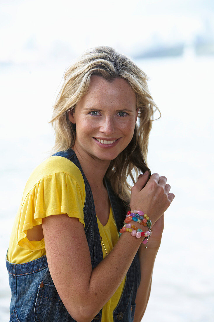 Junge blonde Frau mit gelbem Shirt und Jeansweste im Strand
