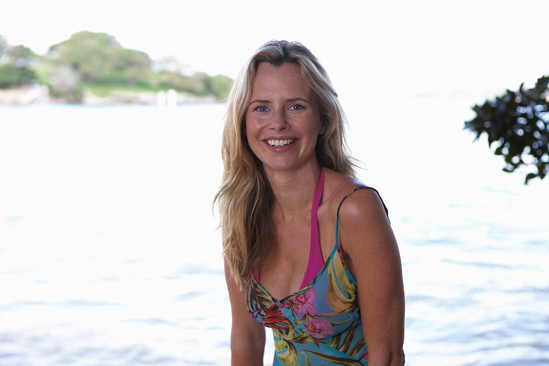 A young blonde woman on a beach wearing a purple bikini top and a summer dress