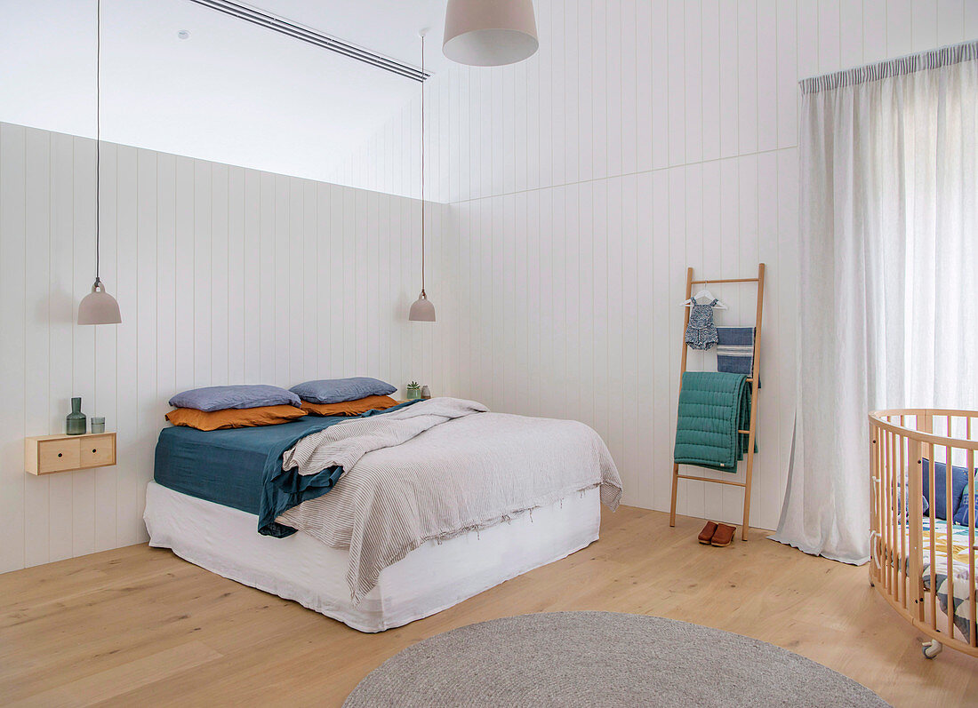 Bett unterm Oberlicht im schlichten Schlafzimmer mit Babybett