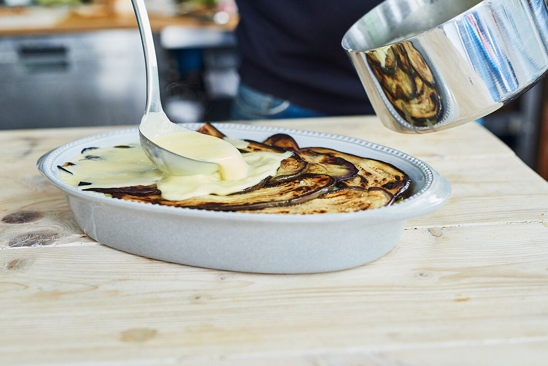 Sauce being poured over moussaka