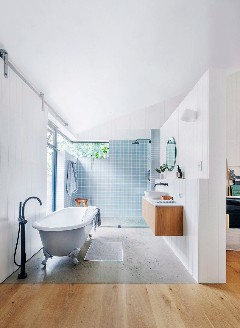 Freestanding bathtub in open bathroom with board wall