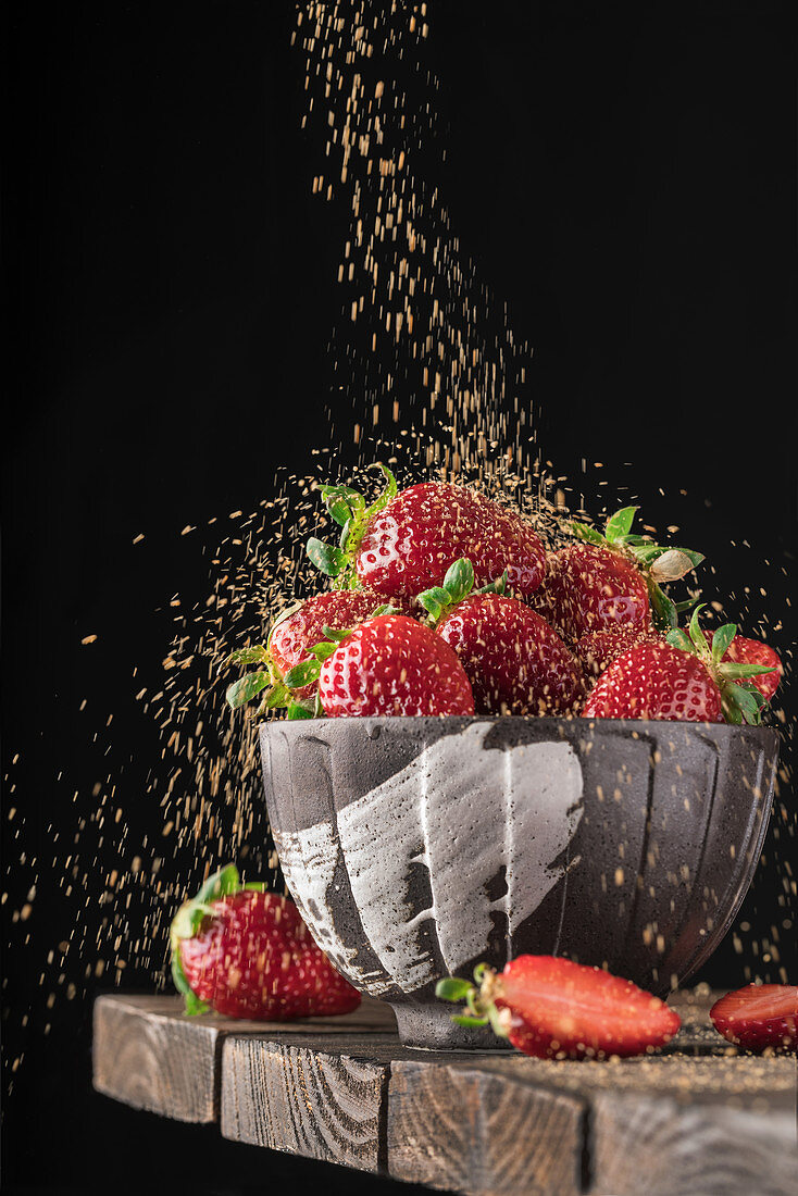 Full bowl of fresh red strawberry in rain of golden crumbs falling