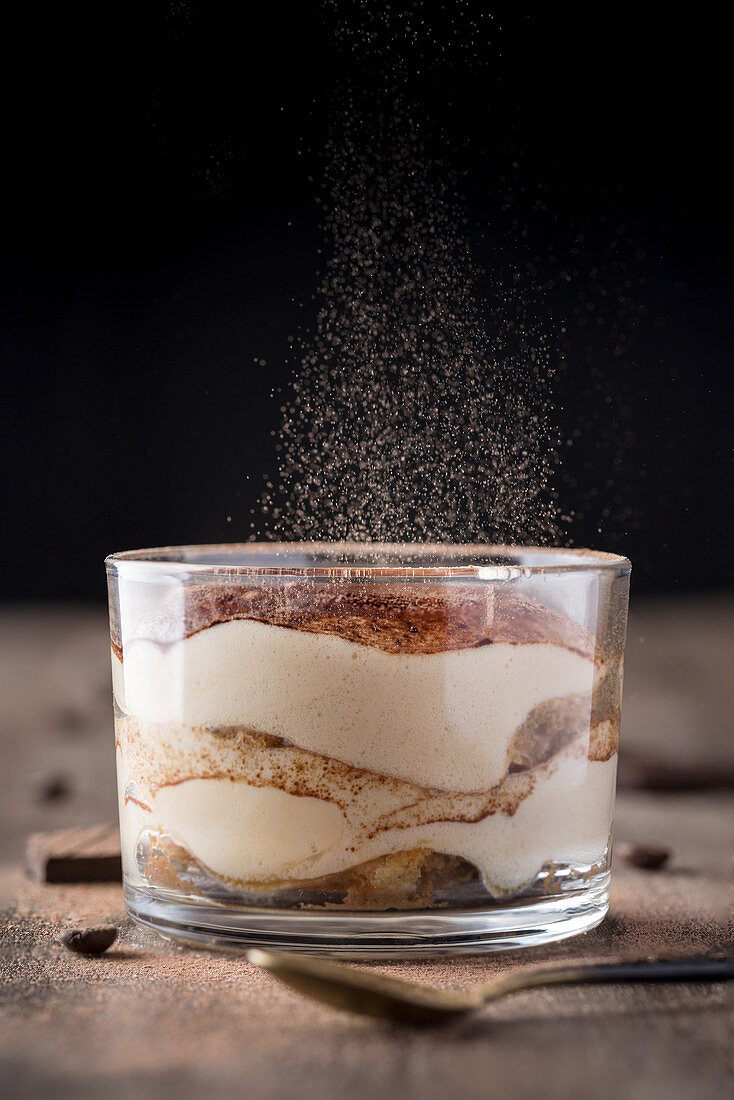 Fresh tiramisu dessert in glass with particles of cocoa dust falling on top