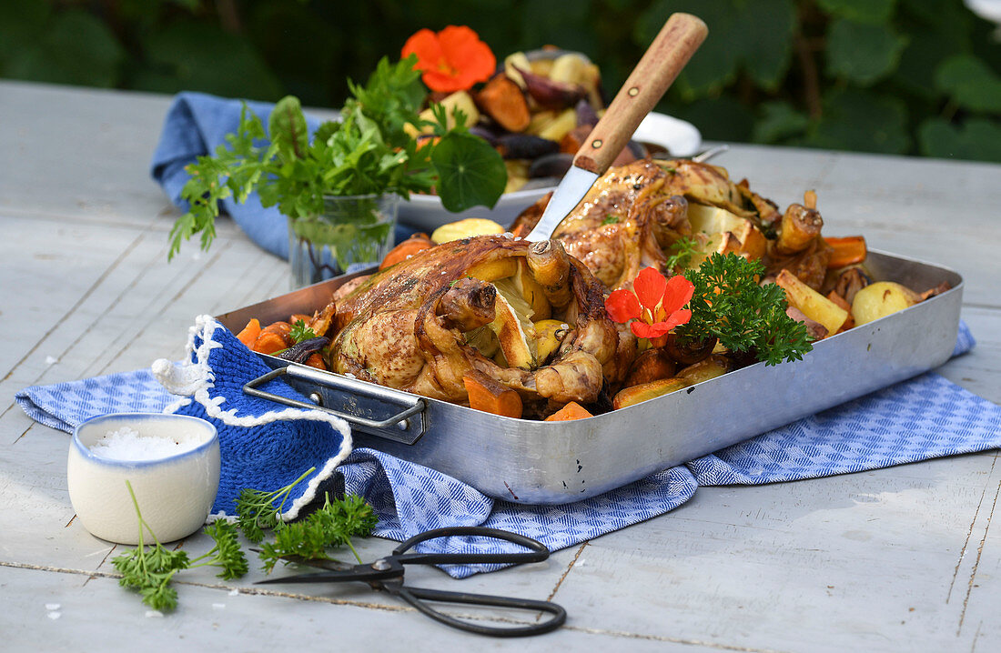 Roast chicken with root vegetables on a table outside