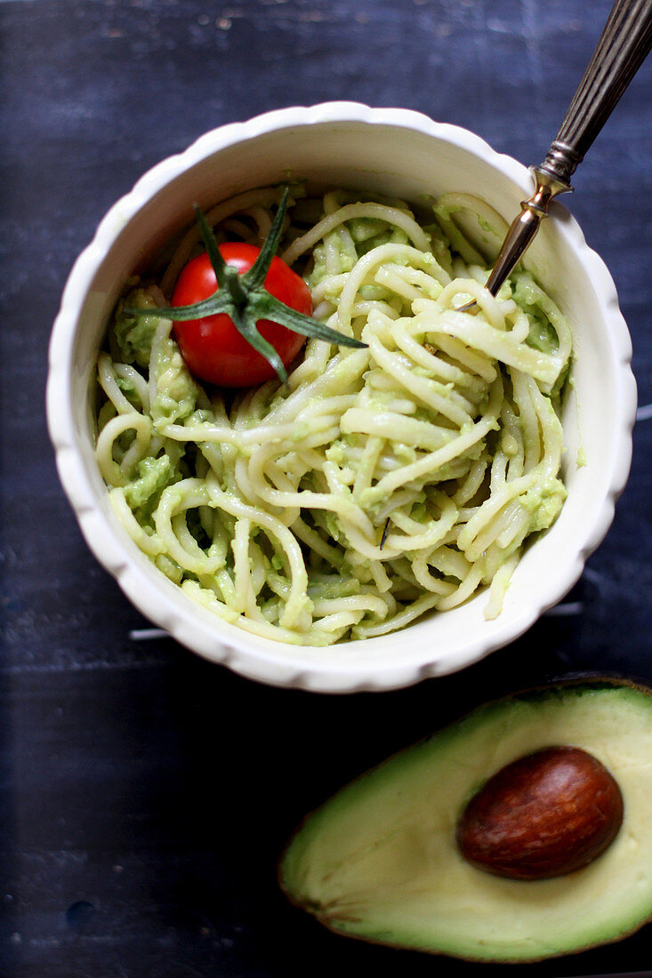 Spaghetti with avocado cream garnished with a cocktail tomato (close up)