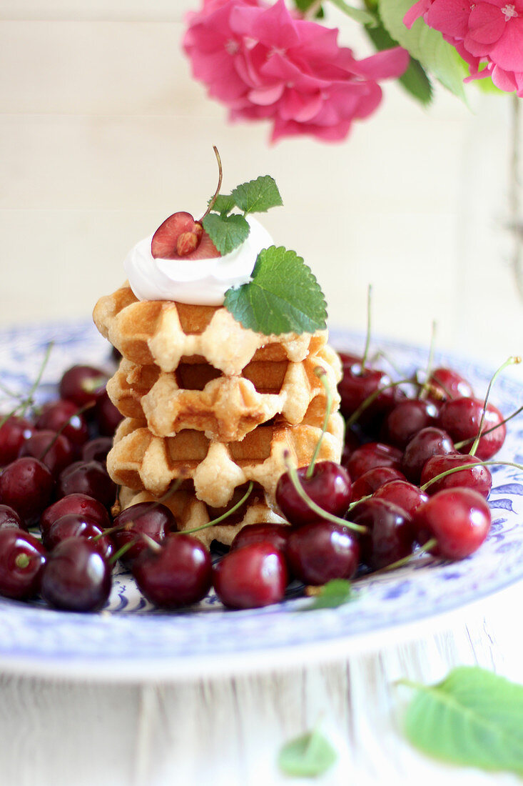 A stack of Belgian waffles with cream and fresh cherries