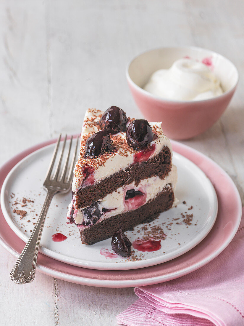 Slice of black forest gateau with cherries and bowl of cream