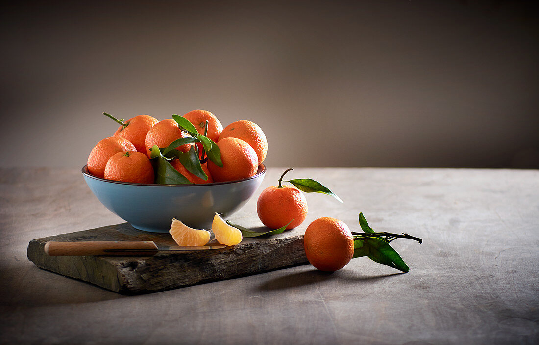 Mandarins in a bowl on a wooden board with a paring knife