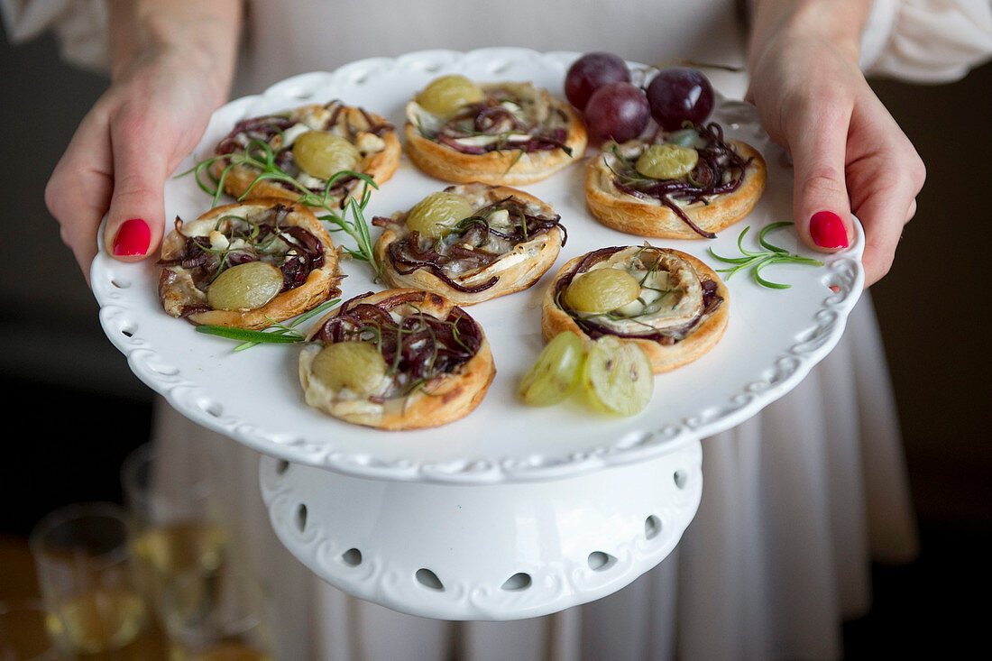 A woman serving mini pizzas with chevre, balsamic onions and grapes