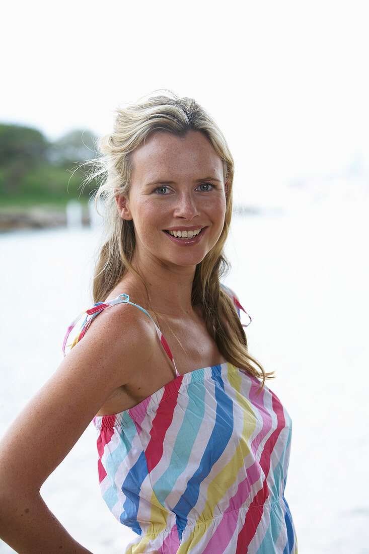 A young blonde woman on a beach wearing a light-blue top