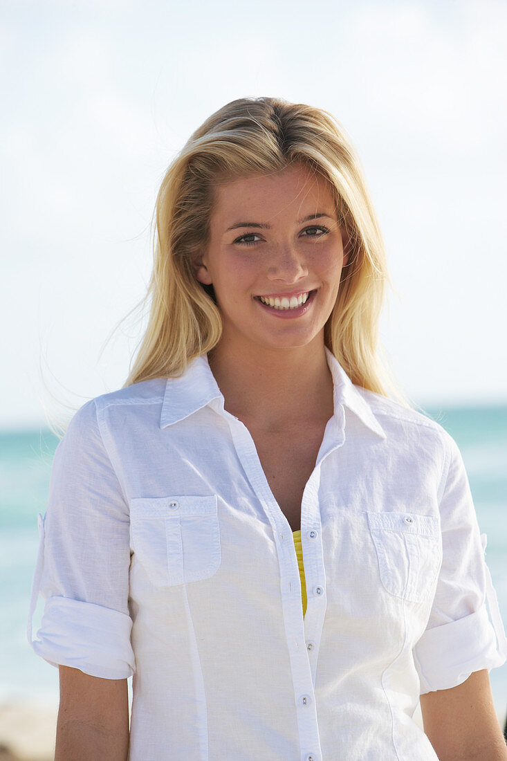 A young blonde woman on a beach wearing a white blouse