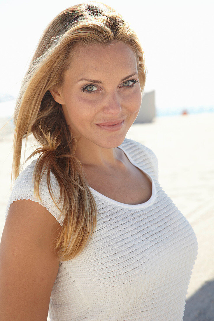 A mature blonde woman on a beach wearing a white top