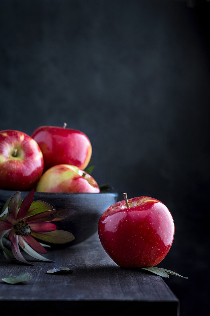 Fresh red apples on wooden table and in a bowl on dark background