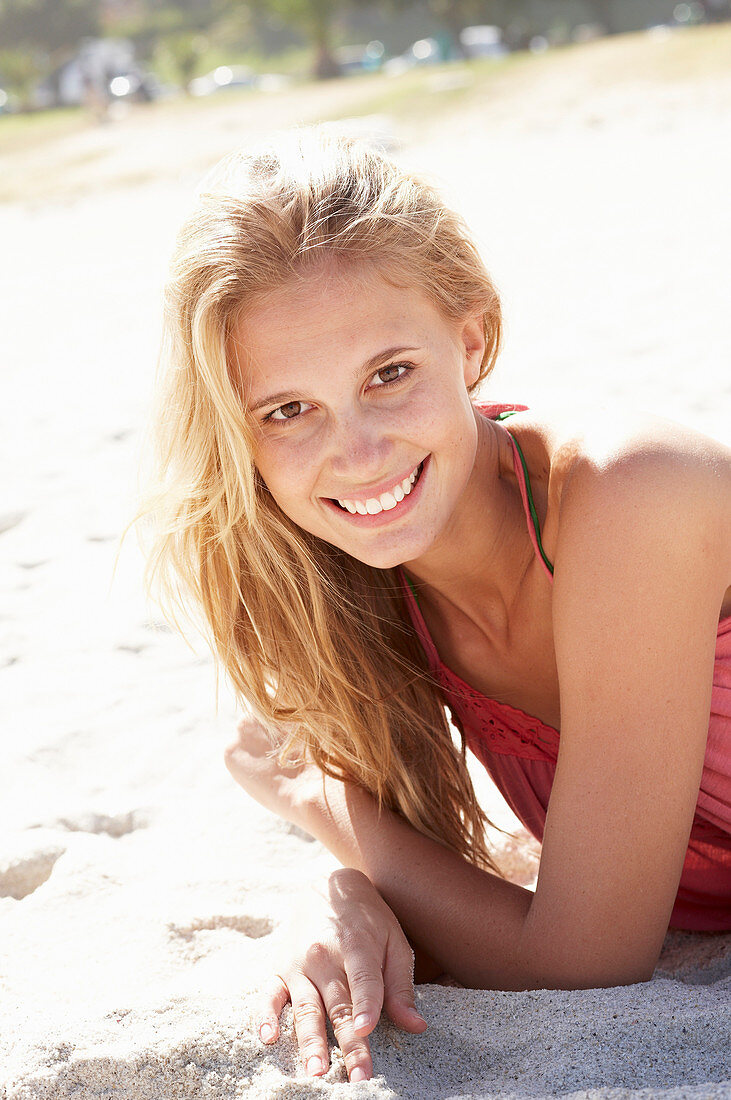 A young blonde woman on a beach wearing a pink top