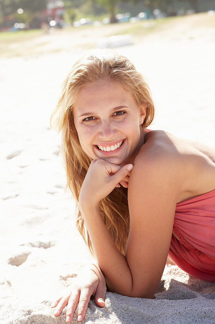 A young blonde woman on a beach wearing a pink top