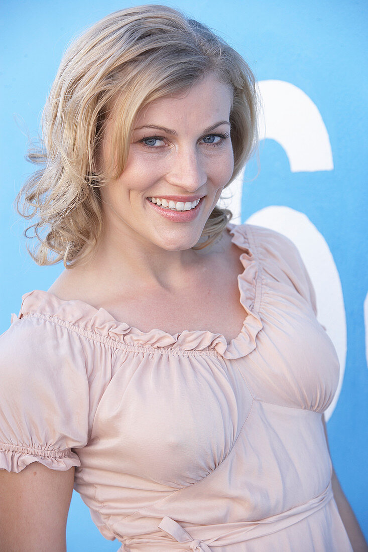 A blonde woman standing against a blue surface wearing a pink short-sleeved blouse