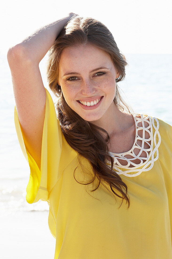 Junge brünette Frau im gelben Sommerkleid am Strand