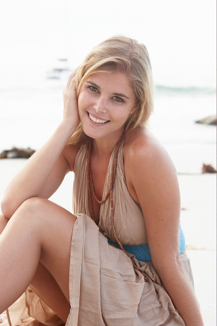 A blonde woman on a beach wearing a beige summer dress