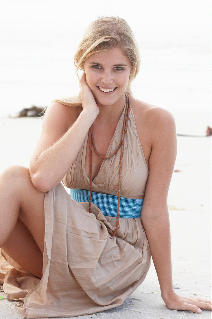 A blonde woman on a beach wearing a beige summer dress