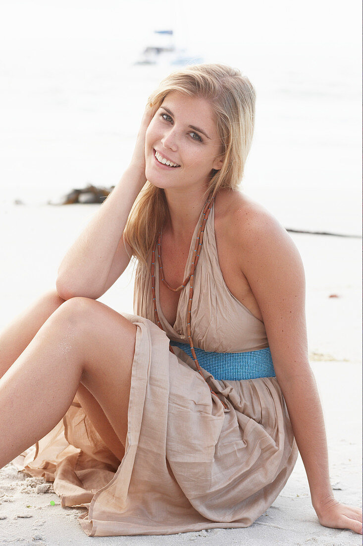 A blonde woman on a beach wearing a beige summer dress