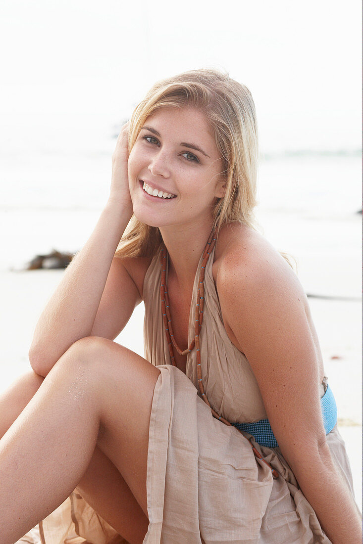 Blonde Frau in beigem Sommerkleid am Strand