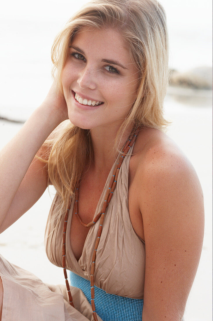 Blonde Frau in beigem Sommerkleid am Strand