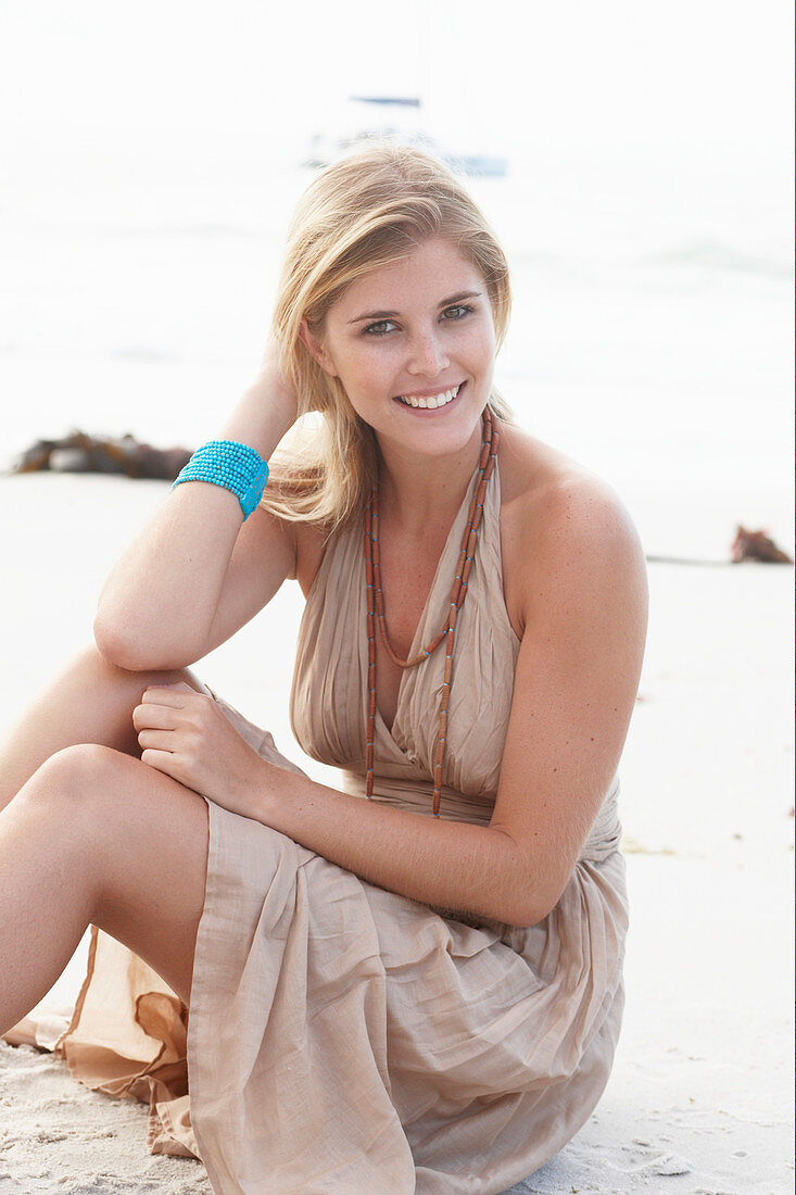 A blonde woman on a beach wearing a beige summer dress