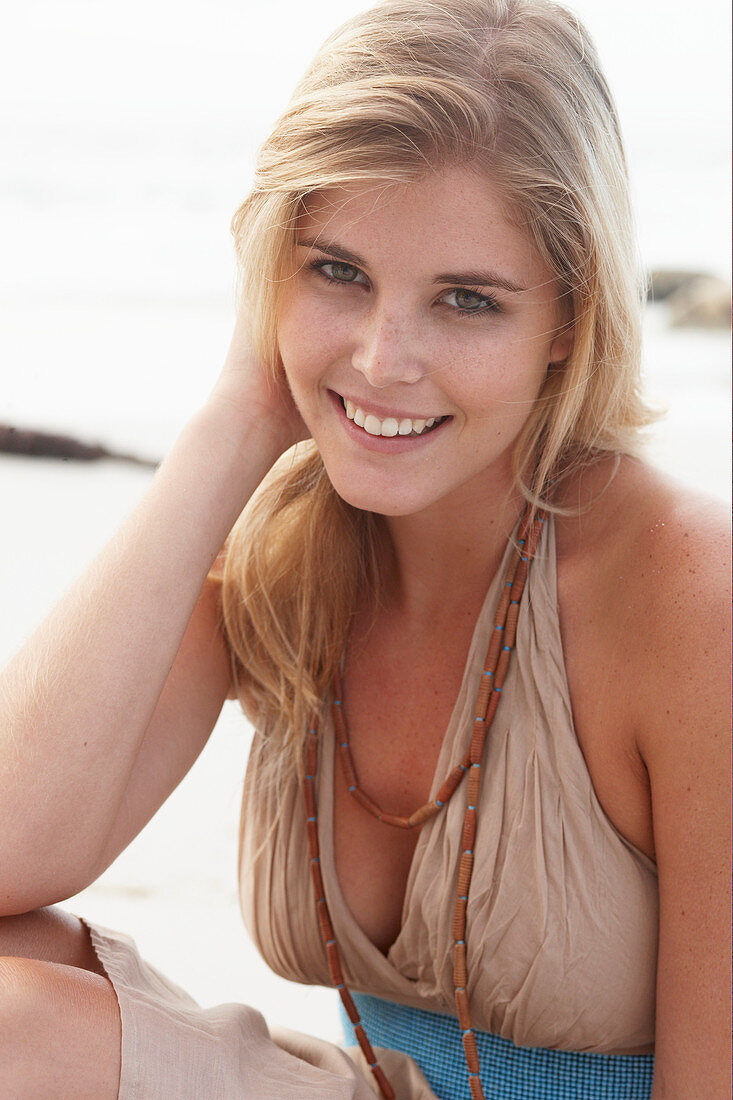 Blonde Frau in beigem Sommerkleid am Strand