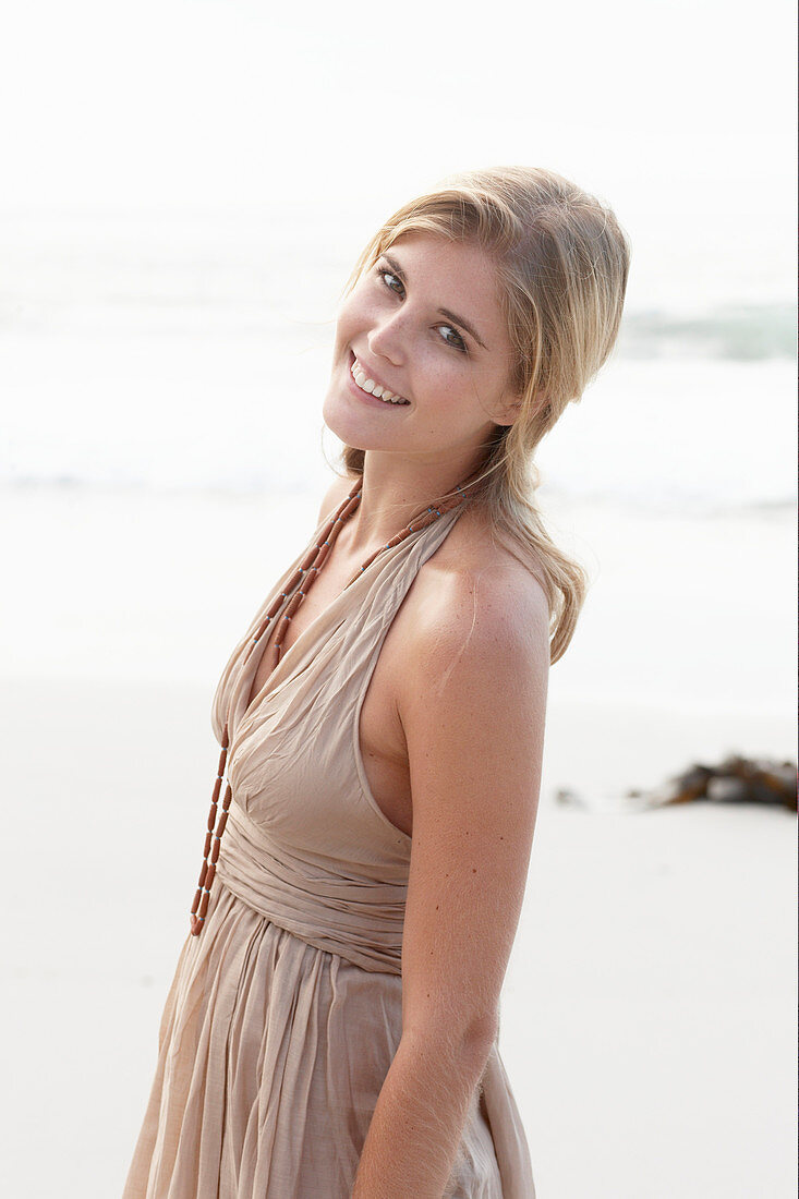 A blonde woman on a beach wearing a beige summer dress