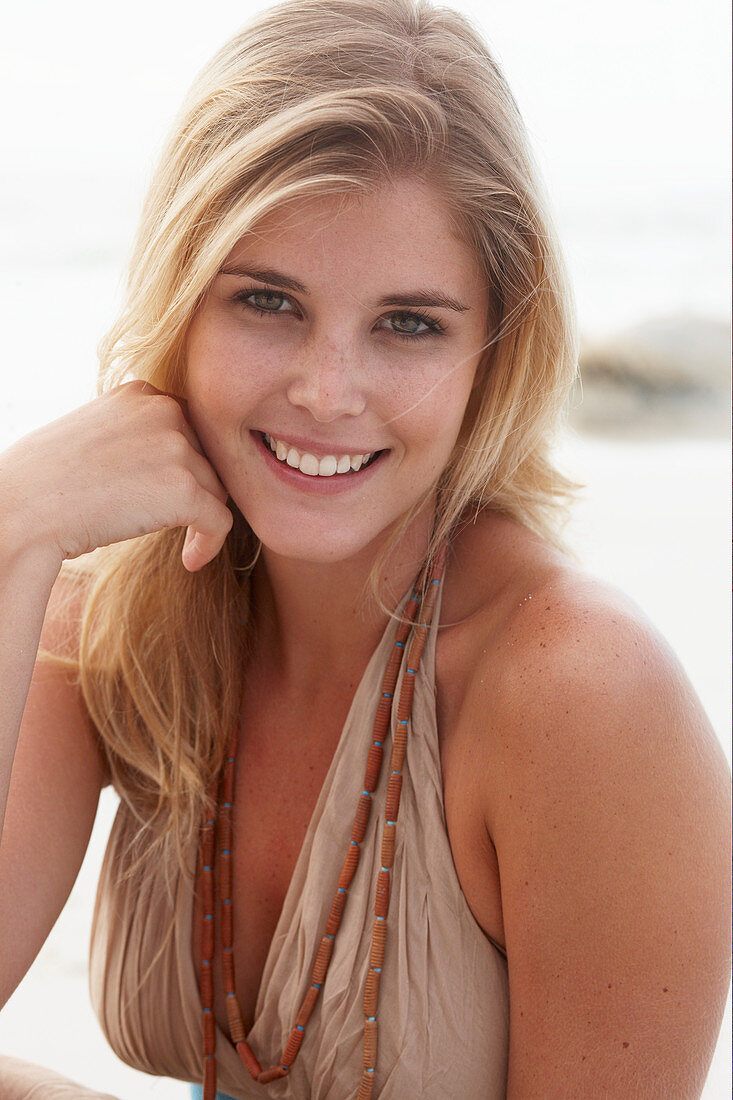 A blonde woman on a beach wearing a beige summer dress