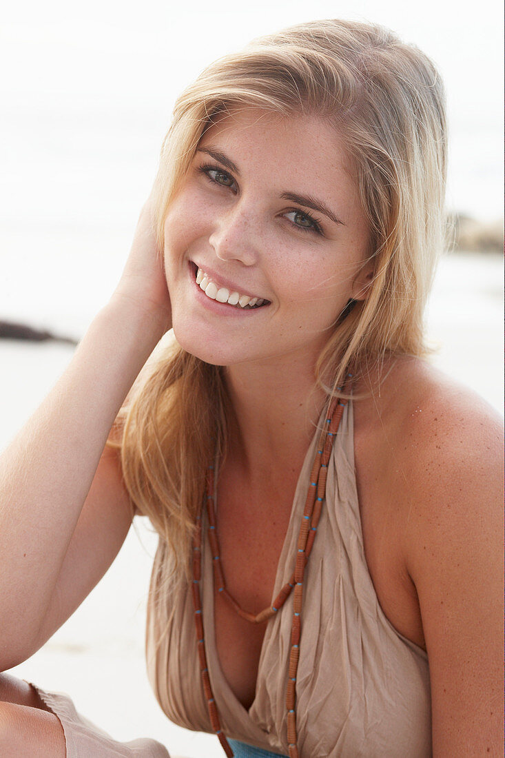 A blonde woman on a beach wearing a beige summer dress